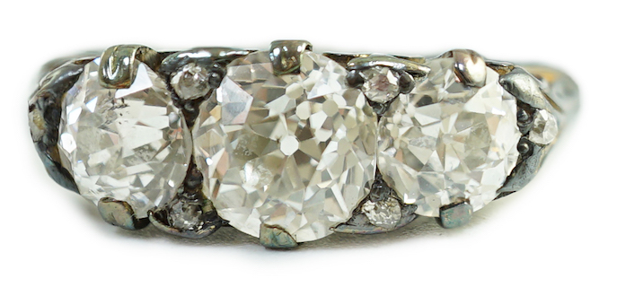 An antique gold, silver and graduated three stone diamond set ring, with diamond chip spacers and diamond chip set shoulders